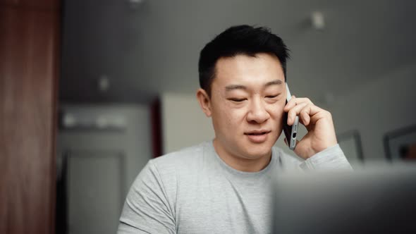 Asian positive man talking by phone and drinking coffee