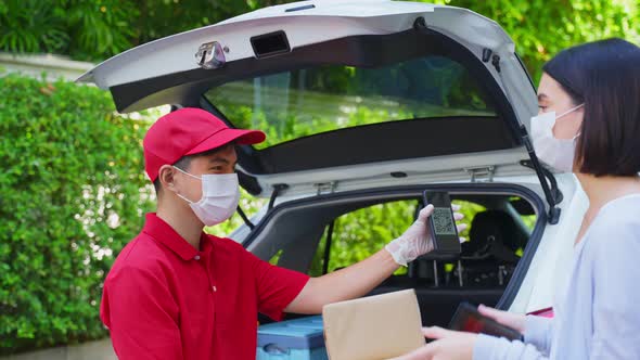 Asian deliver man wearing face mask in red uniform handling parcel box give to woman customer.