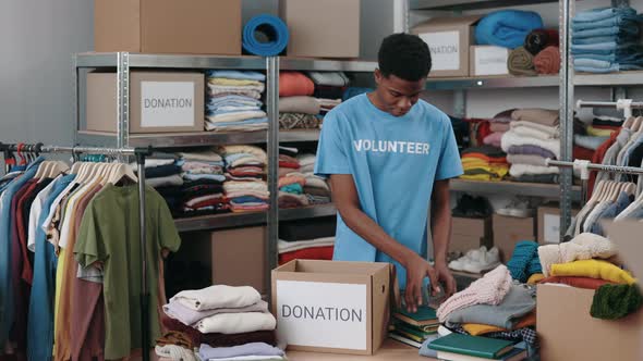 Multiracial Brunette Male Volunteer Sorting Books and Putting It Into the Cupboard Box at the