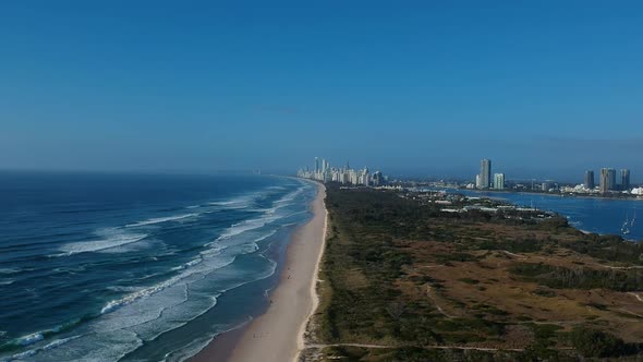 Aerial view of a coastline near a large area of green space with a sprawling city skyline in the dis