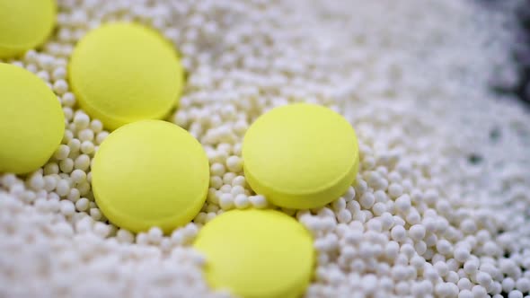 Yellow Round Pills Falling Into Granules Scattered on a Black Background Closeup