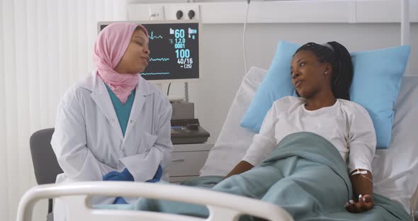 Muslim Woman Doctor Taking Care of Young Female Patient Lying in Medical Hospital Bed