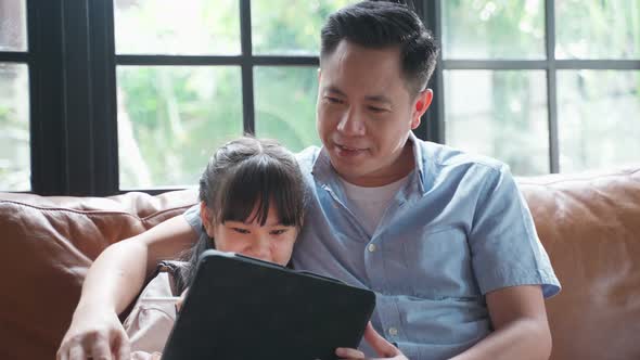Asian family girl kid and father use tablet playing internet online together in living room at home.