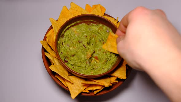 Man Hand taking some fried nachos in a pot with some fresh guacamole from clay dishes on white