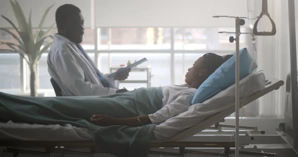 African Male Doctor Checking Up Female Patient in Hospital Ward