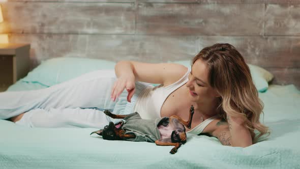 Caucasian Young Woman in Pajamas Smiling While Playing with Her Dog