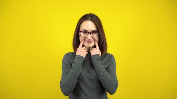 A Young Woman Makes a Cheerful Smile on Her Face with Her Fingers on a Yellow Background. Woman with