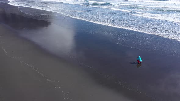 Aerial View of a Female Traveler Photographing Atlantic Ocean Waves on the Beach. Hofn, Iceland