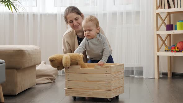 Little baby boy with mother collecting toys in wooden toy box