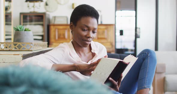 Happy african american woman sitting on sofa in living room, reading book