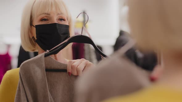 Closeup Mature Woman in Protective Mask in Clothing Store Looks in Mirror Trying on Elegant Dress