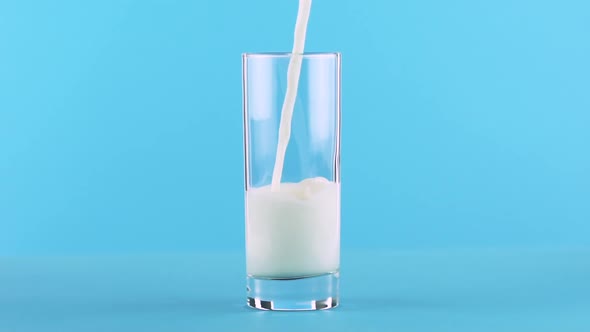 Slow Motion Close-up Shot of Milk Cold Beverage Drink Pooring Into Glass Blue Background in Studio