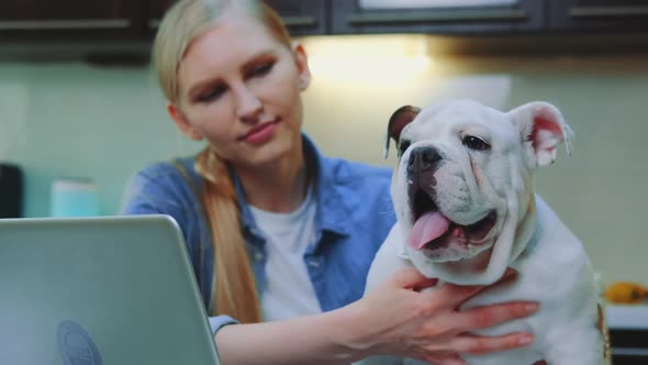 Woman Petting Bulldog Sitting on Table Near Laptop