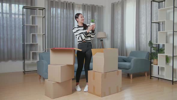 Young Asian Woman Moving Into A New House Unpacking The Cardboard Box And Taking Stuff Out Of It