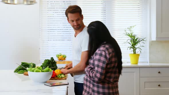 Pregnant woman talking to man while cutting vegetable 