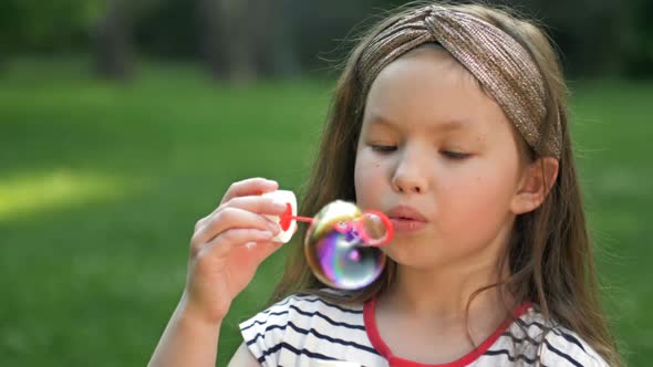 Cute Little Girl is Blowing a Soap Bubbles