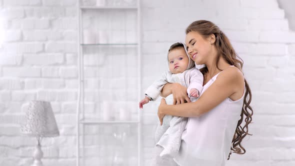 Pleasant Beautiful Mother Hugging Little Baby Having Best Feeling Enjoying Morning at White Room