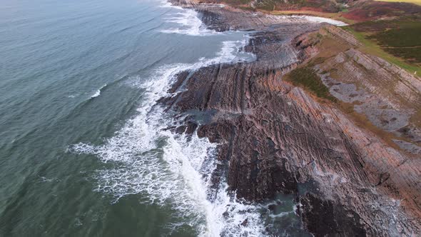 AERIAL: Fly towards along textured rocky coastline with crashing waves, Port Eynon Gower, 4k Drone