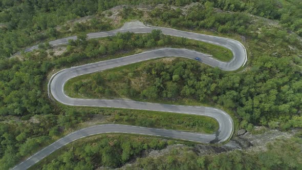 Blue Car Is Going on Mountain Winding Road in Norway. Green Forest. Aerial Vertical Top-Down View