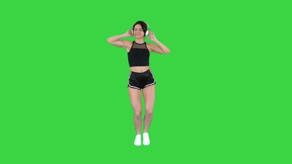 Young Happy Sportive Woman Listening Music in Headphones and Dancing on a Green Screen, Chroma Key.