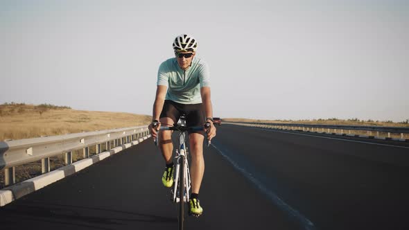 Confident Male Cyclist in Glasses and Helmet Rides Bicycle Along Track and Lets Go of His Hands