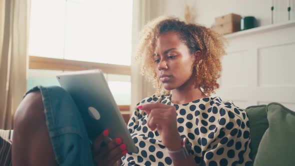 Young African American Woman Uses Tablet Computer Sits on Sofa in Living Room