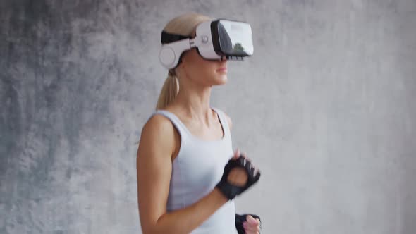 Young and sporty girl in sportswear is doing exercises at home using virtual reality helmet.