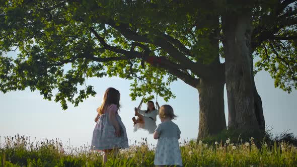 Sisters Walking Near Clean Green Field To Their Mother, Swinging on Swing Tied To an Old Oak-tree.