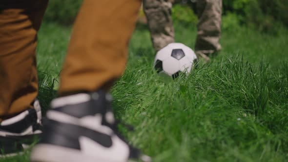 Unrecognizable Teenage Boy and Military Woman Passing Soccer Ball in Slow Motion on Green Spring