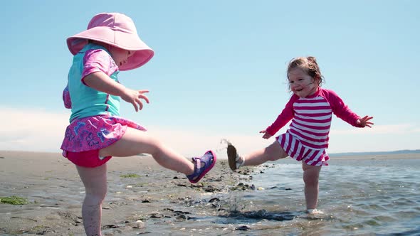 Two Baby Girls Splashing Water On Sandy Beach
