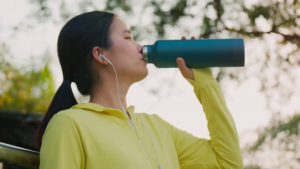 A beautiful caucasian woman athlete drinks water after running at the park.