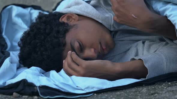 Freezing African-American refugee lying on street in sleeping bag