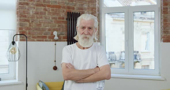 Senior Bearded Man with Wrinkled Face in Home Clothes Poses on Camera 
