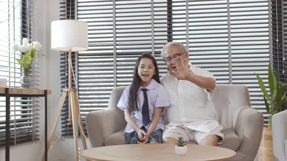 Happy family little daughter and grandpa sitting on the sofa make video call chatting use electronic