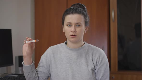 Sad Young Woman Showing Thermometer Touching Forehead with Hand Sighing Looking at Camera