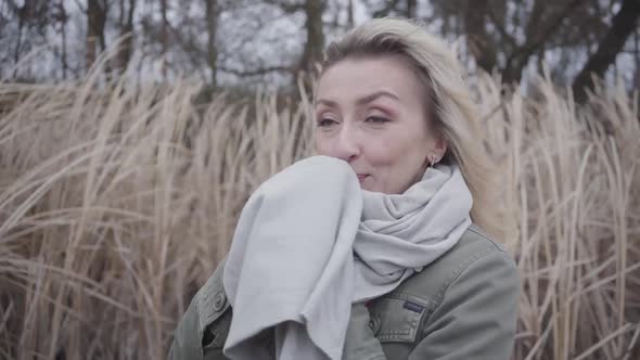 Portrait of Young Beautiful Woman Standing in Cold Wind. Charming Girl with Blond Hair and Brown