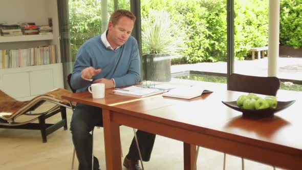 Wide shot of male at dinning table looking at personal finance