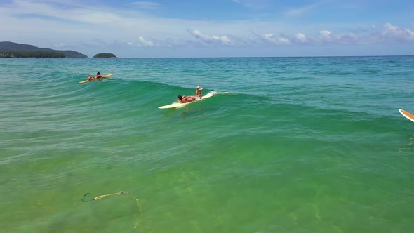 4K Aerial view group of Asian woman surfing in the sea at tropical beach.