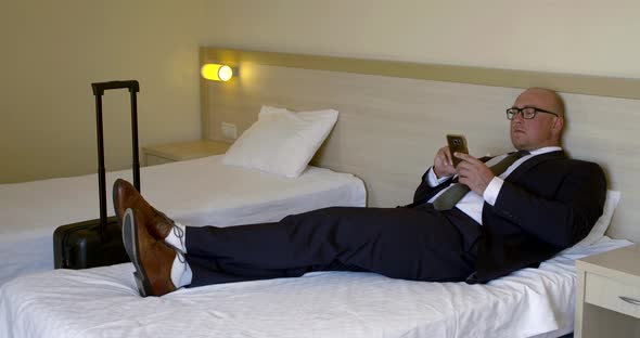 Man Is Lying on Bed in Hotel Room and Playing Game in Smartphone in Business Trip