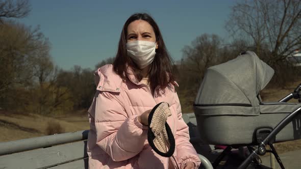 Young Mother with a Stroller Basking in the Autumn Sun and Waving a Knitted Headband