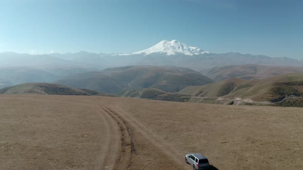 Amazing View From Highland To Snowy Peak Elbrus Peak. Travel SUV Car Standing on Off Road Field with