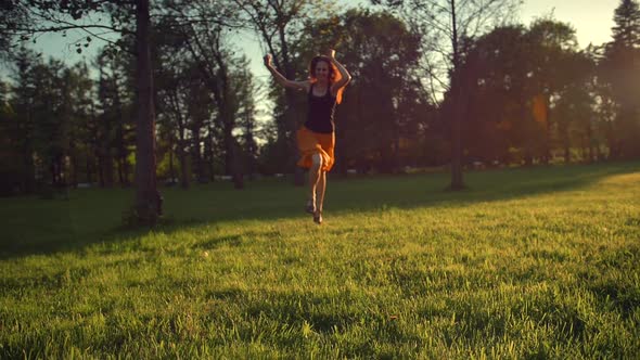 Young Woman Dancing Running and Jumping on Grass in Park at Sunset.