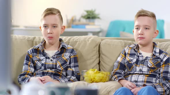 Caucasian Twins Watching TV and Eating Crisps in Unison alt
