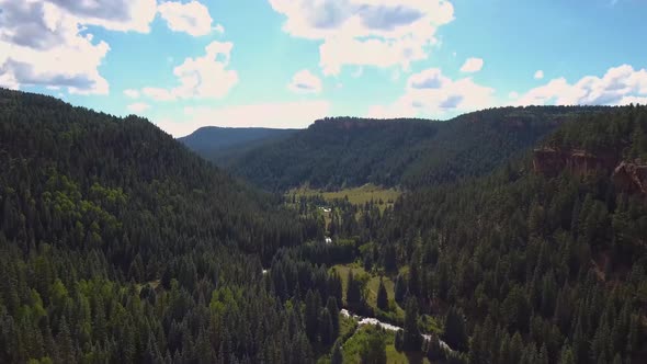 AERIAL: Tilt downward to reveal the stream running through this valley of evergreen trees.