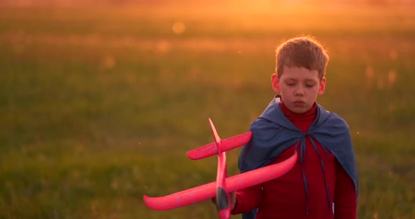 The Boy Runs Across the Field with a Plane in His Hands at Sunset