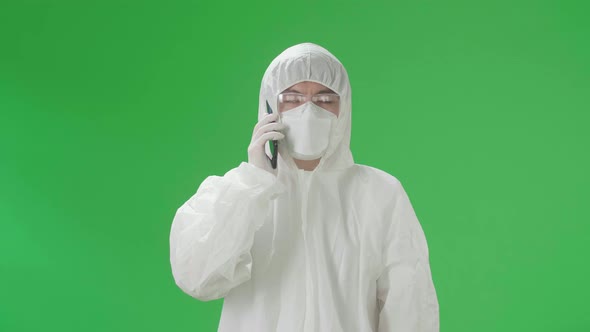 Asian Man Wear Protective Uniform PPE And Talking On Mobile Phone In The Green Screen Studio