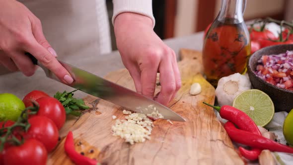 Woman Slices Garlic on a Kitchen Board Using a Knife