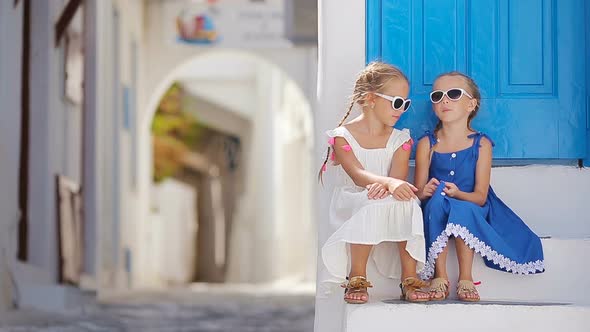 Two Girls in Blue Dresses Having Fun Outdoors. Kids at Street of Typical Greek Traditional Village