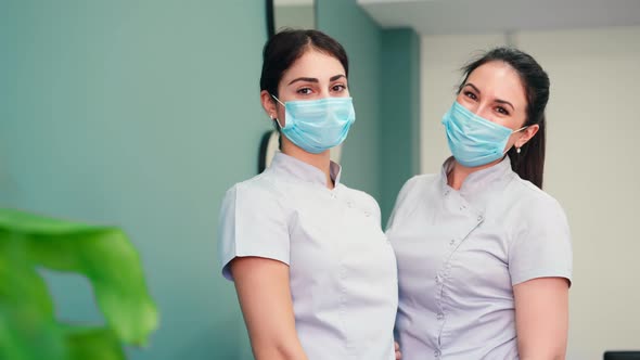 Two Beautiful Nurses in Medical Masks Smile for the Camera in the Hospital