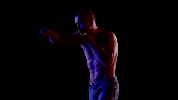 a Muscular Bald Man with a Bare Torso and Jeans is Fighting a Shadow on a Black Background